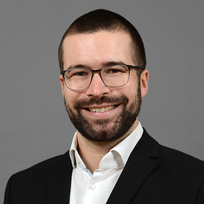 Portraitfoto von Philipp Lukas. Er hat kurze dunkle Haare und einen Bart. Er trägt ein Brille. Er hat weiße Haufarbe. Er trägt ein schwarzes Sakko und ein weißes Hemd.