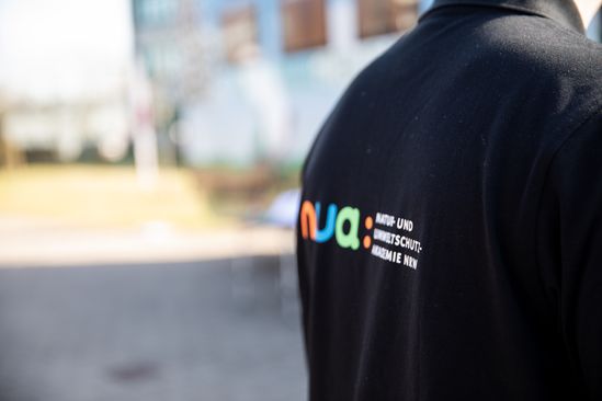 Rücken einer Person, die ein scharzes Shirt mit dem NUA-Logo trägt.